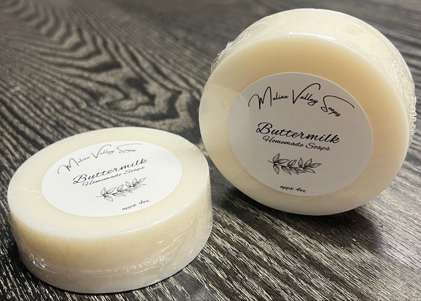 Two round soap bars with labels on a wooden surface. 