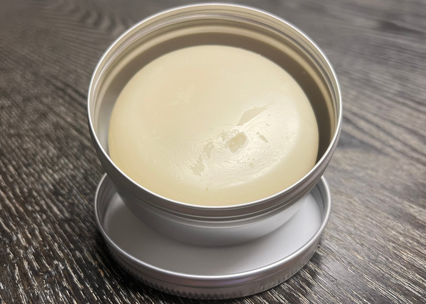 Beige lotion bar in a metal tin on a wooden surface. 