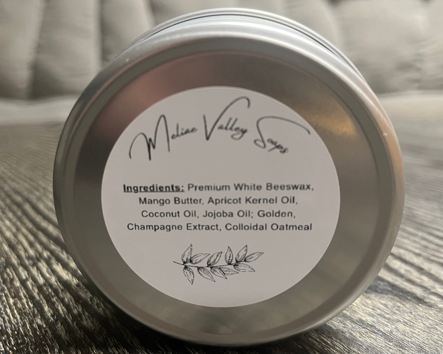 Tin of lotion bar with a white ingredients label on a wooden surface. 