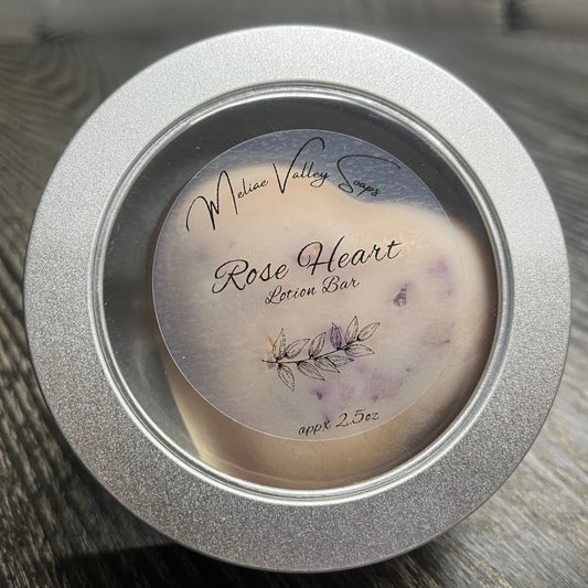 Heart-shaped pink lotion bar with visible rose petals in a tin with a clear label.