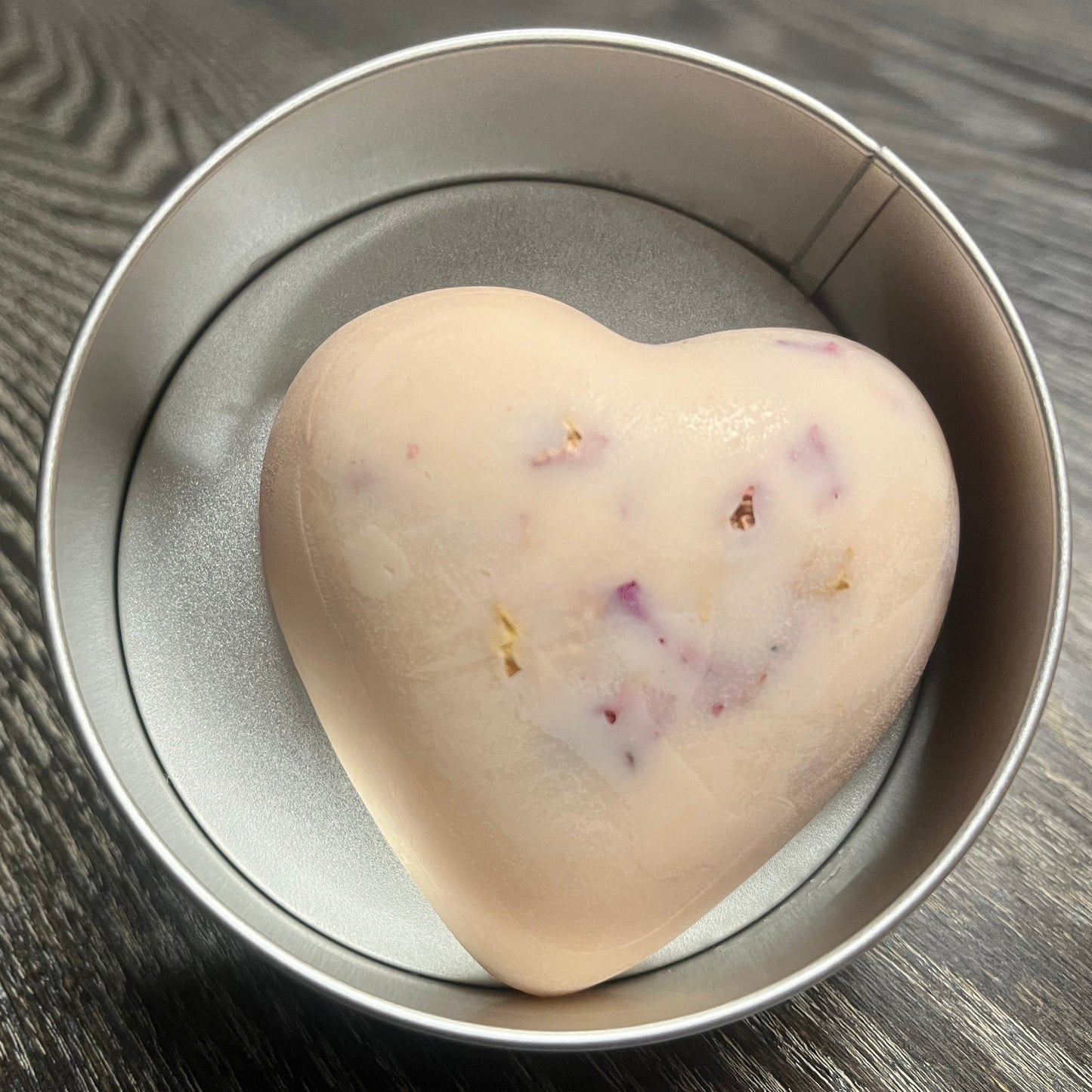 Heart-shaped pink lotion bar with visible rose petals in a tin.