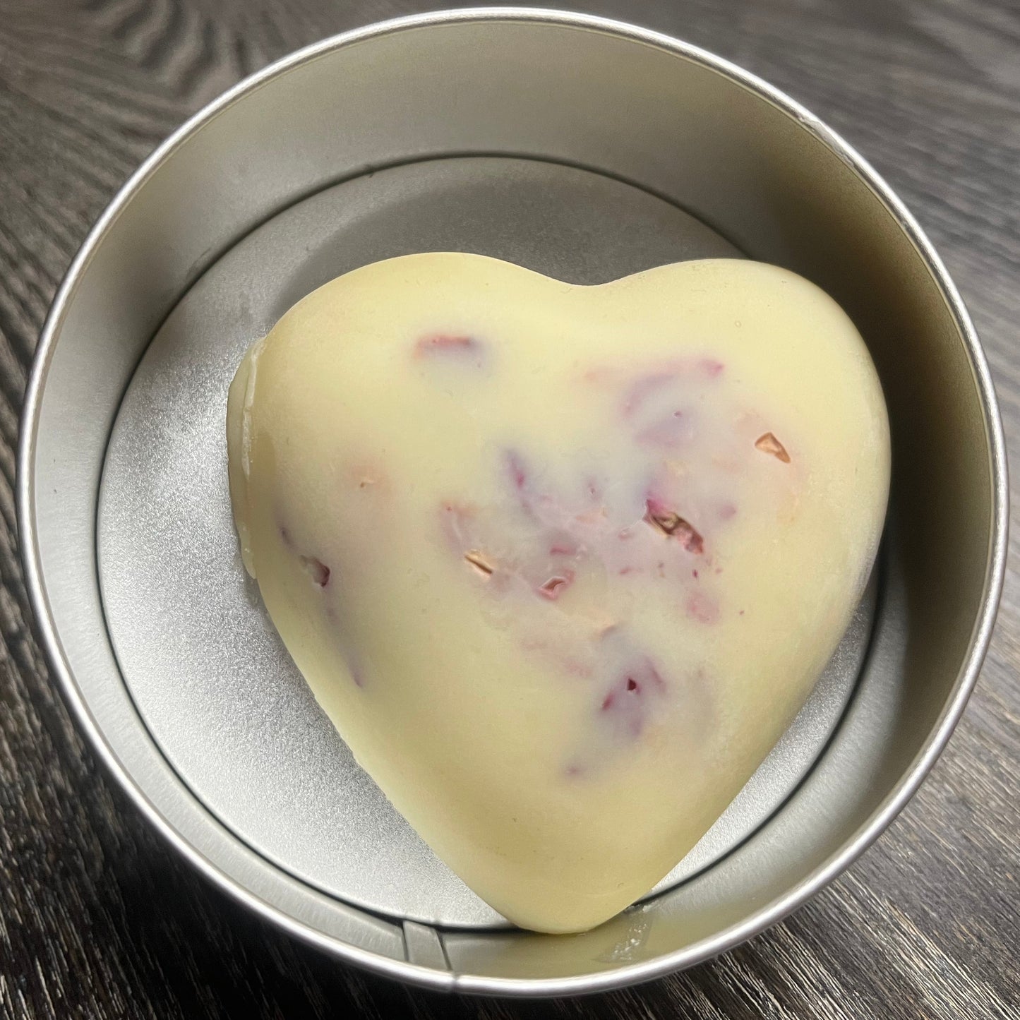 Heart-shaped white lotion bar with visible rose petals in a tin.