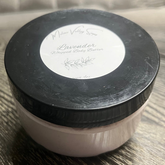 Jar of lavender body butter with a black lid and a white label on a wooden surface.