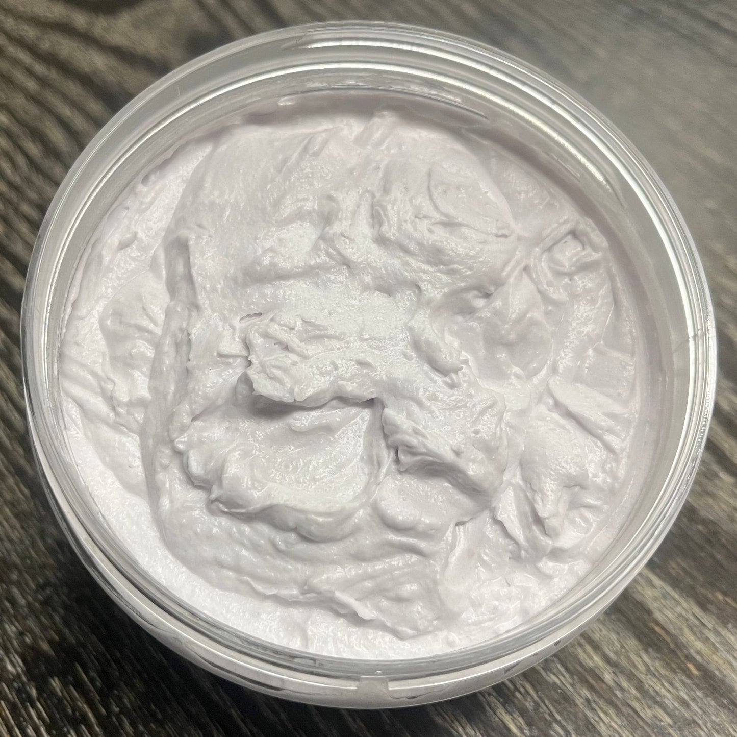 Lavender whipped body butter in a clear jar on a wooden surface. 