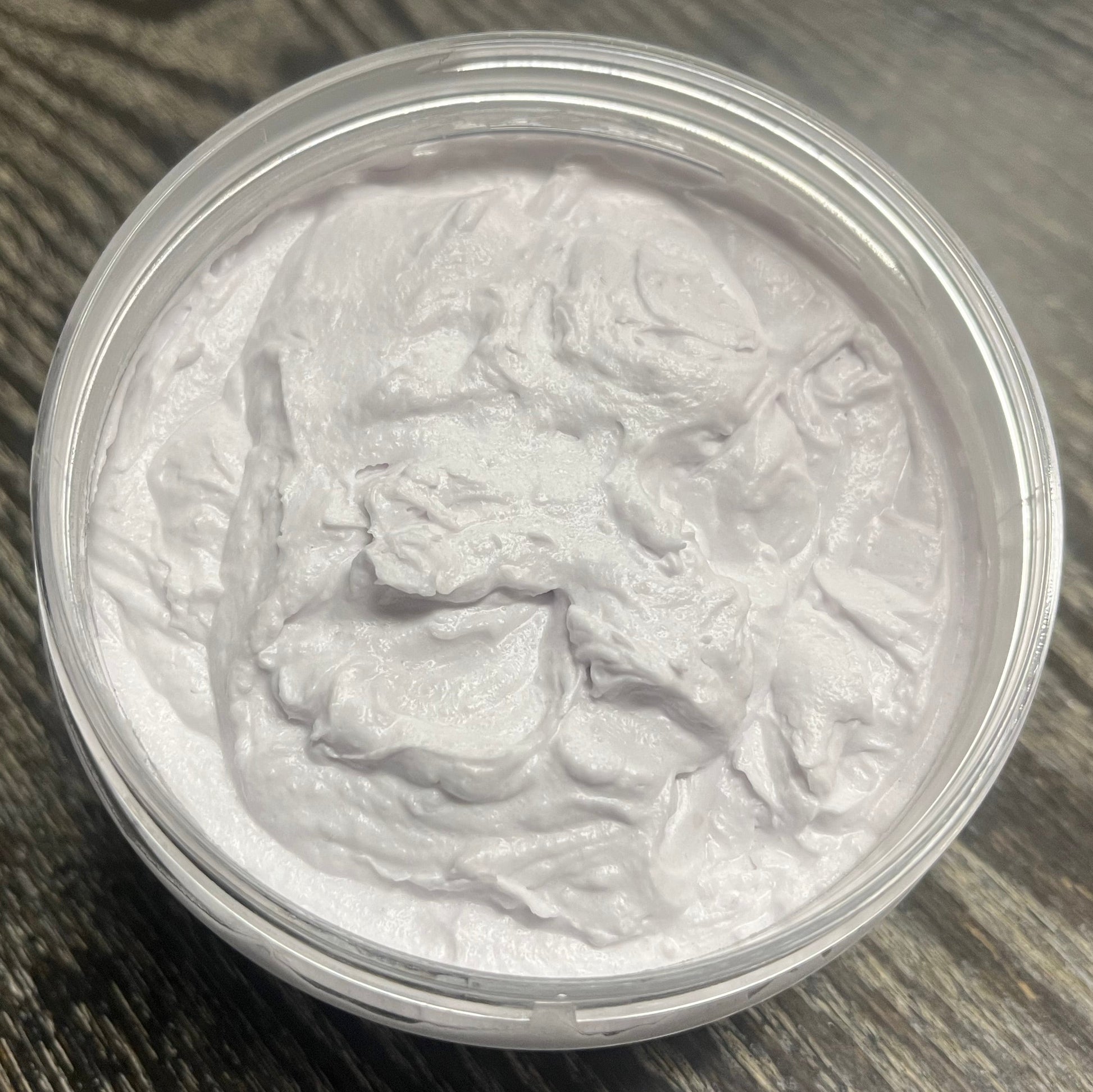 Lavender whipped body butter in a clear jar on a wooden surface. 