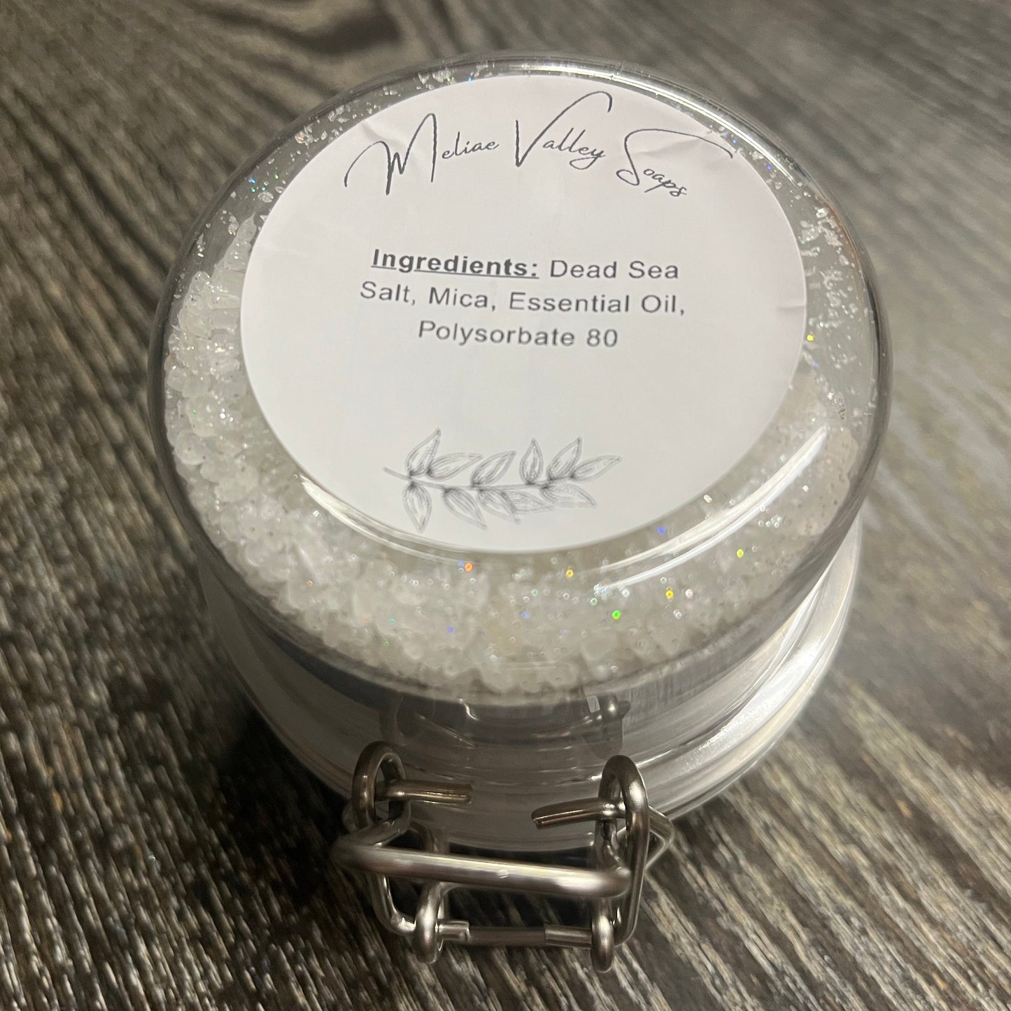 Jar of dead sea salt with a white ingredients label on a wooden surface. 