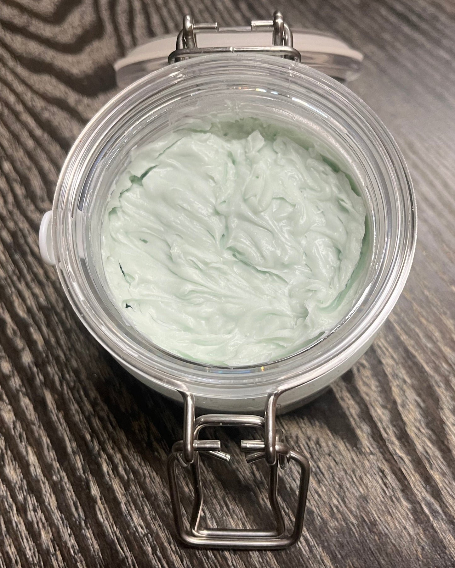 Jar of green whipped body butter on a wooden surface. 