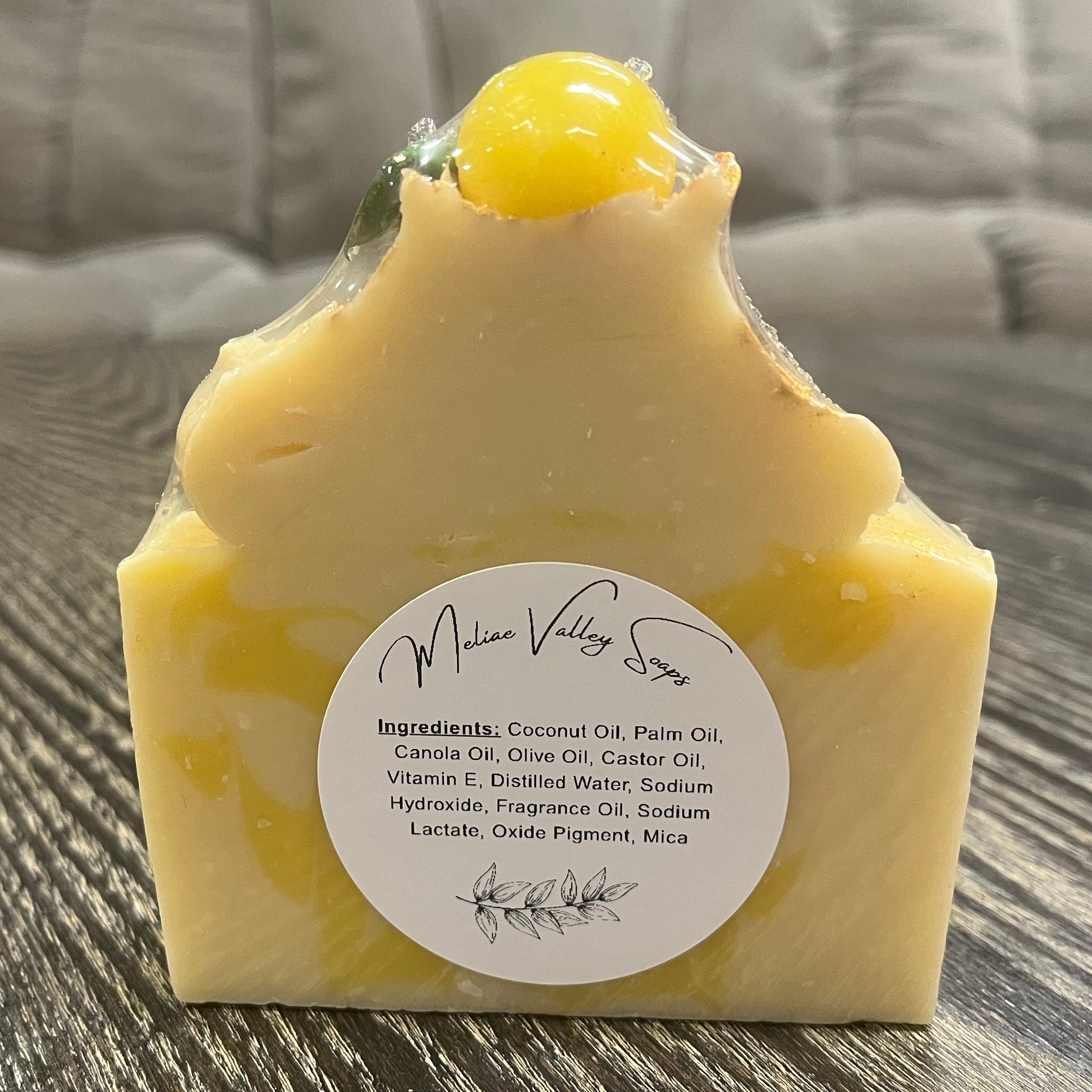 Yellow soap bar with a white ingredients label on a wooden surface. 