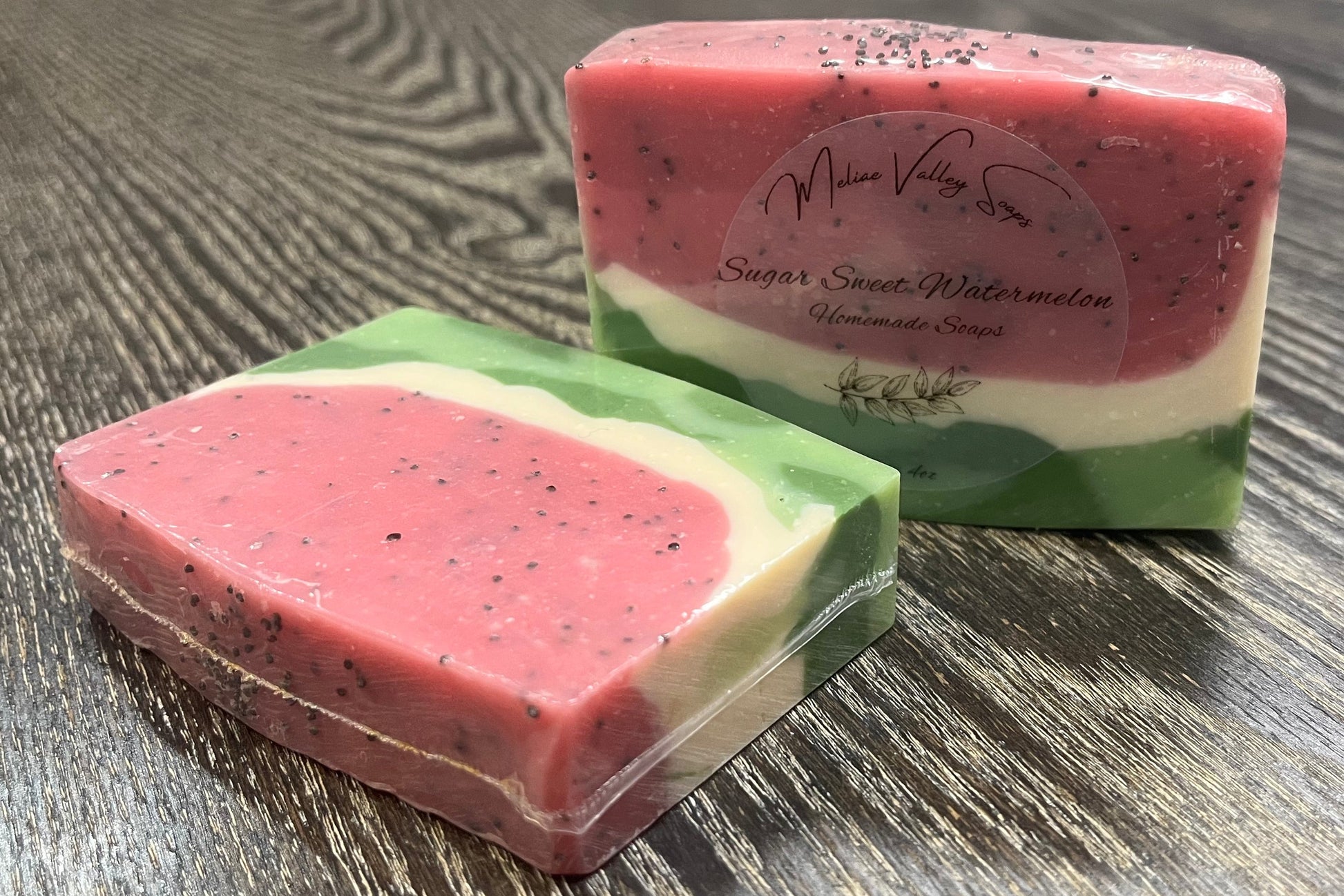 Two bars of pink and green soap on a wooden surface. 