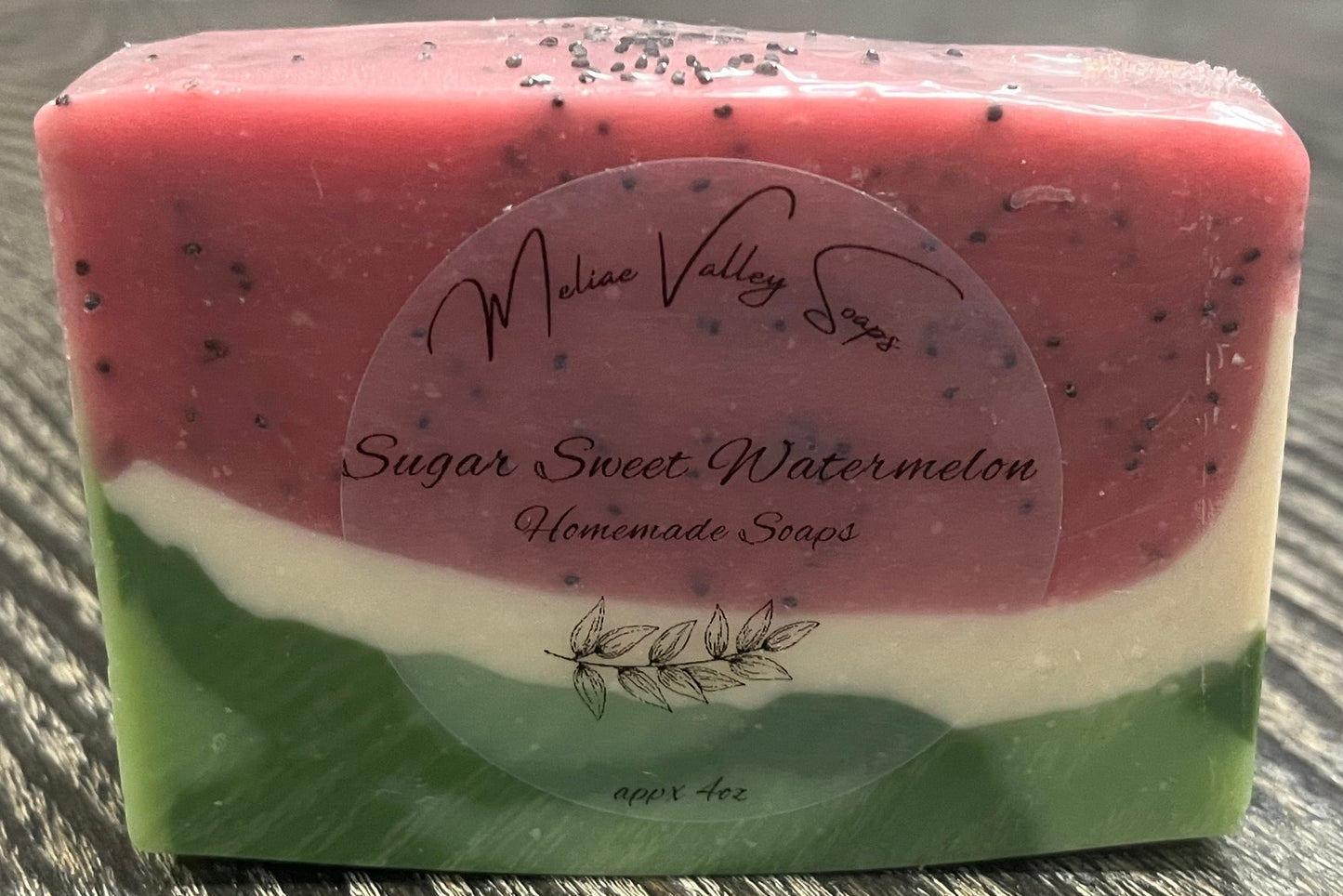 A bar of pink, white, and green soap with a label on a wooden surface. 
