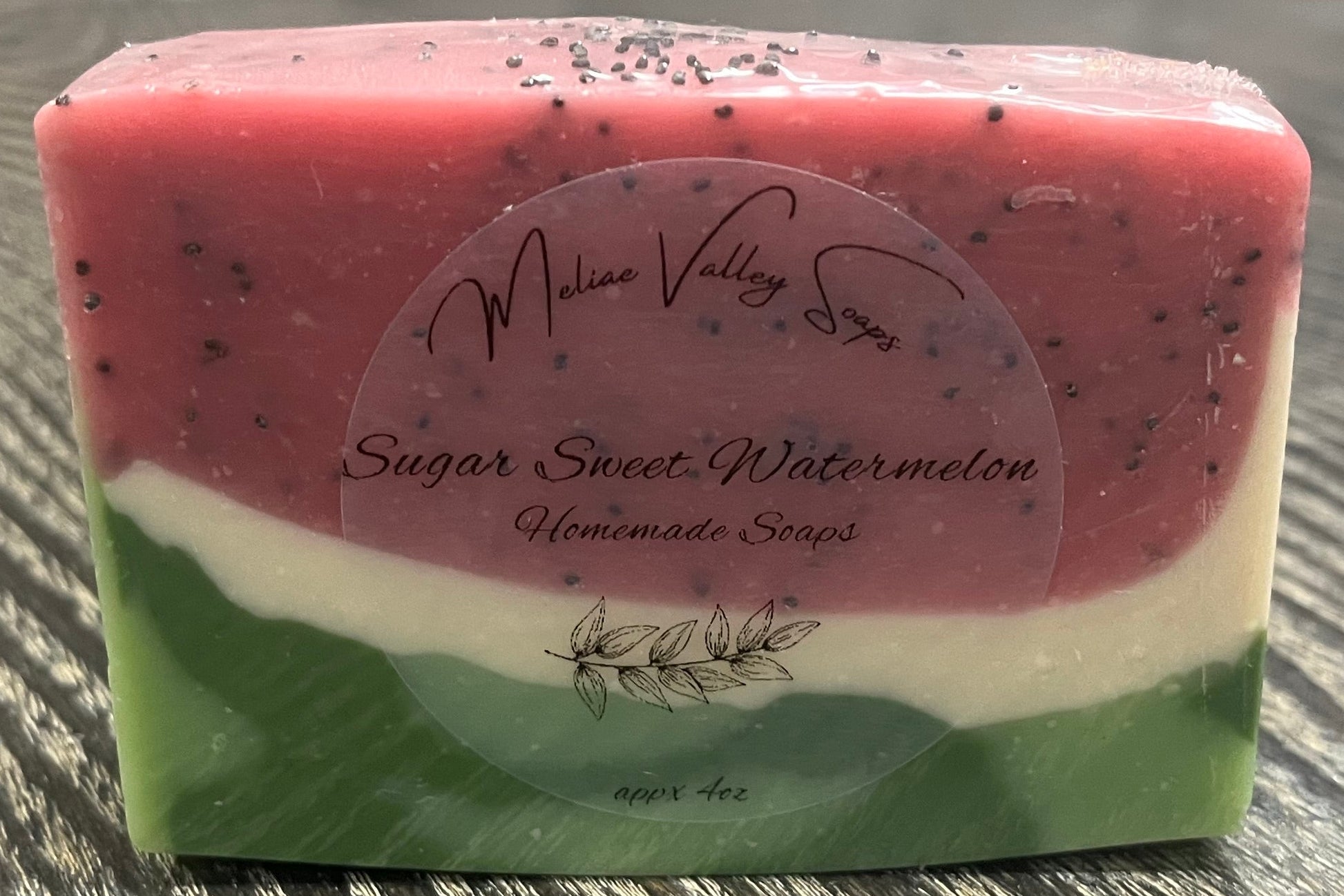 A bar of pink, white, and green soap with a label on a wooden surface. 
