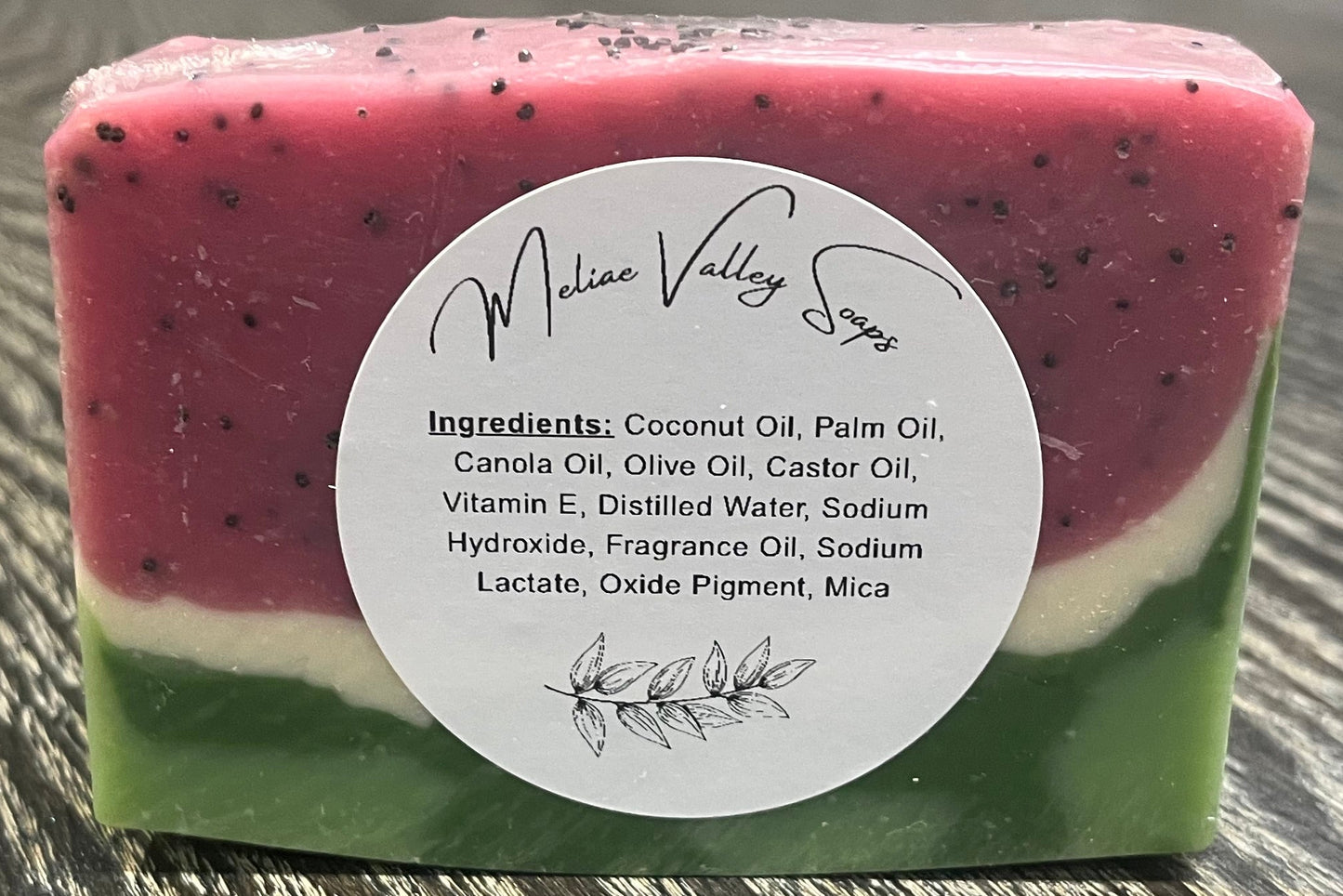 Watermelon-patterned soap bar with a white ingredients label on a wooden surface. 