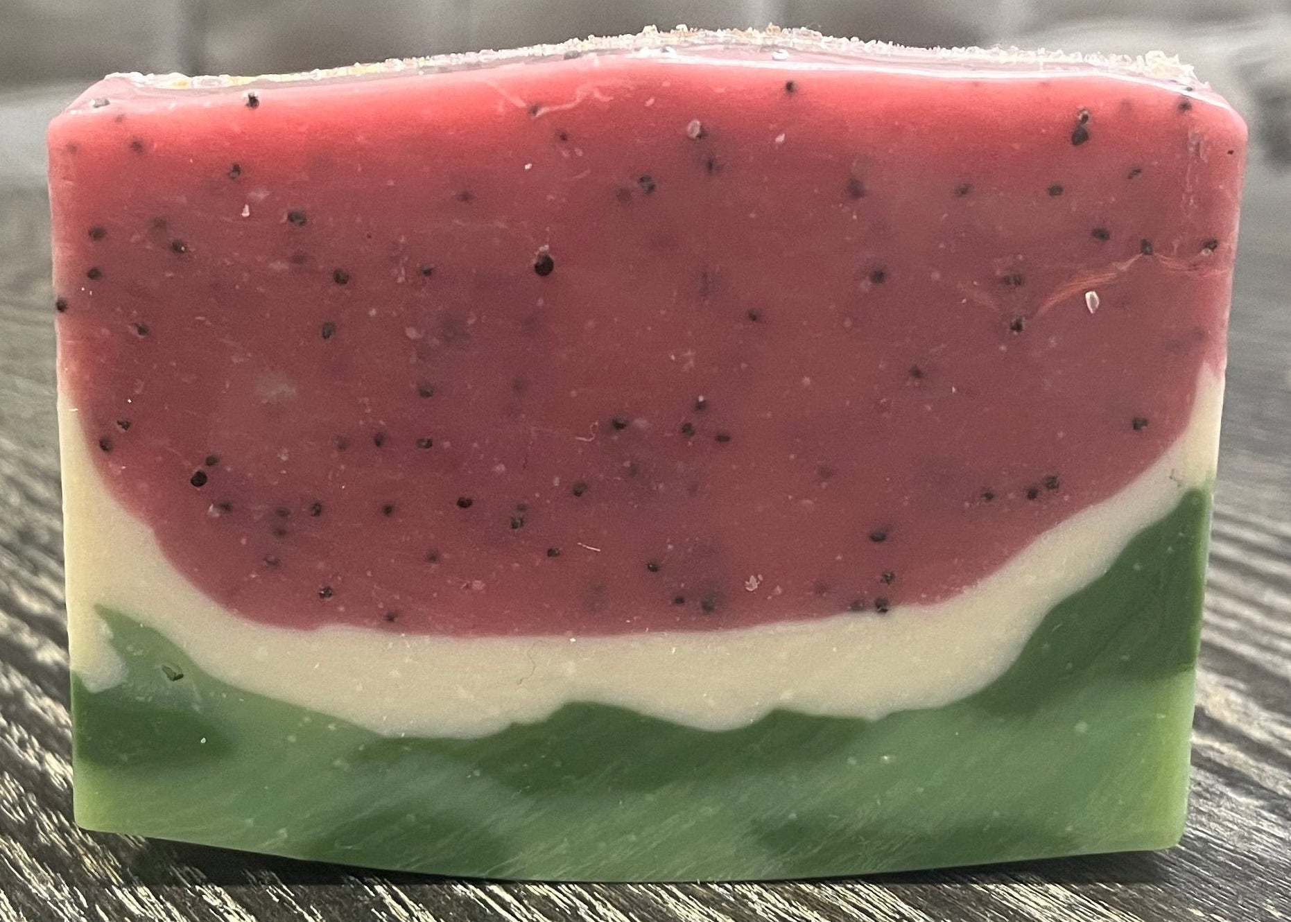 Bar of soap with watermelon pattern on a textured surface. 