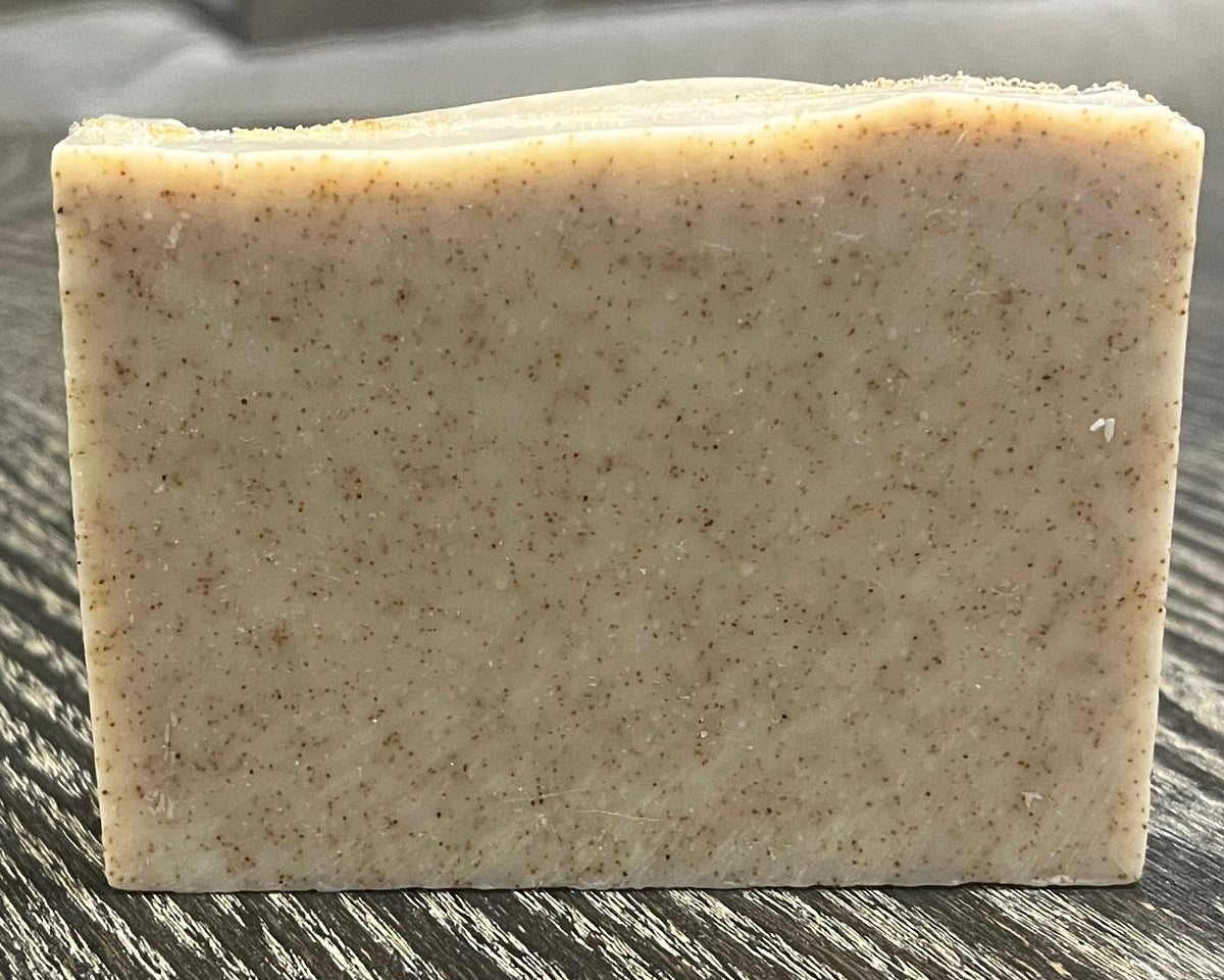 A beige soap bar with darker brown specs of ground walnut shells. 