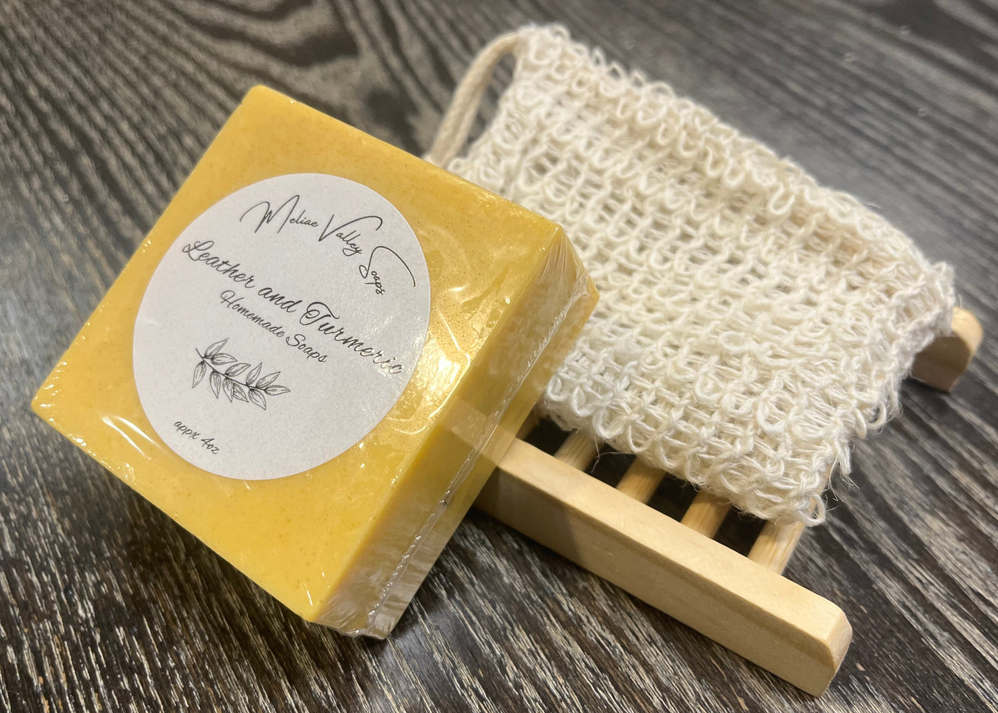A yellow soap with a wooden stand and exfoliating bag on a dark wooden surface. 