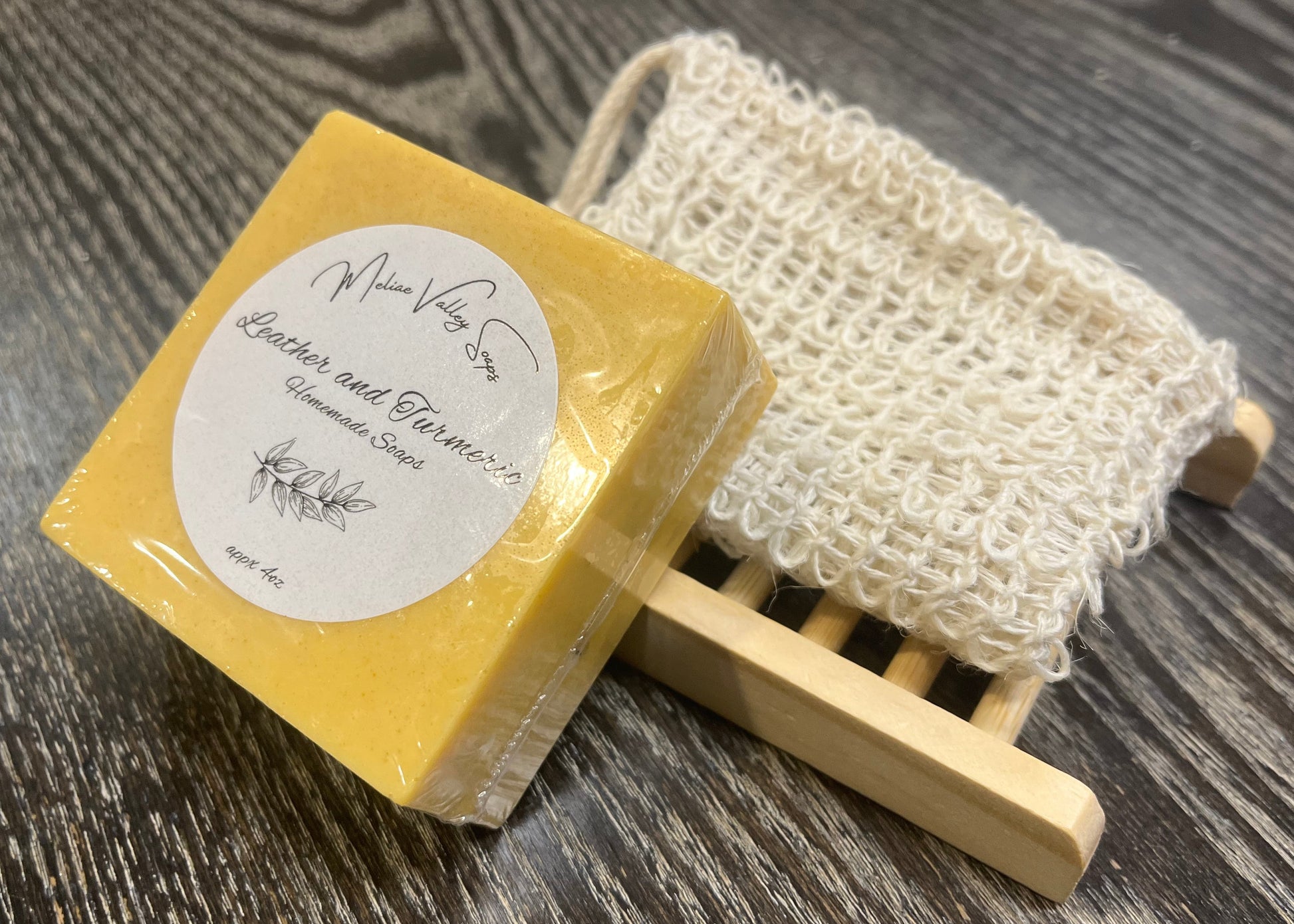 A yellow soap with a wooden stand and exfoliating bag on a dark wooden surface. 