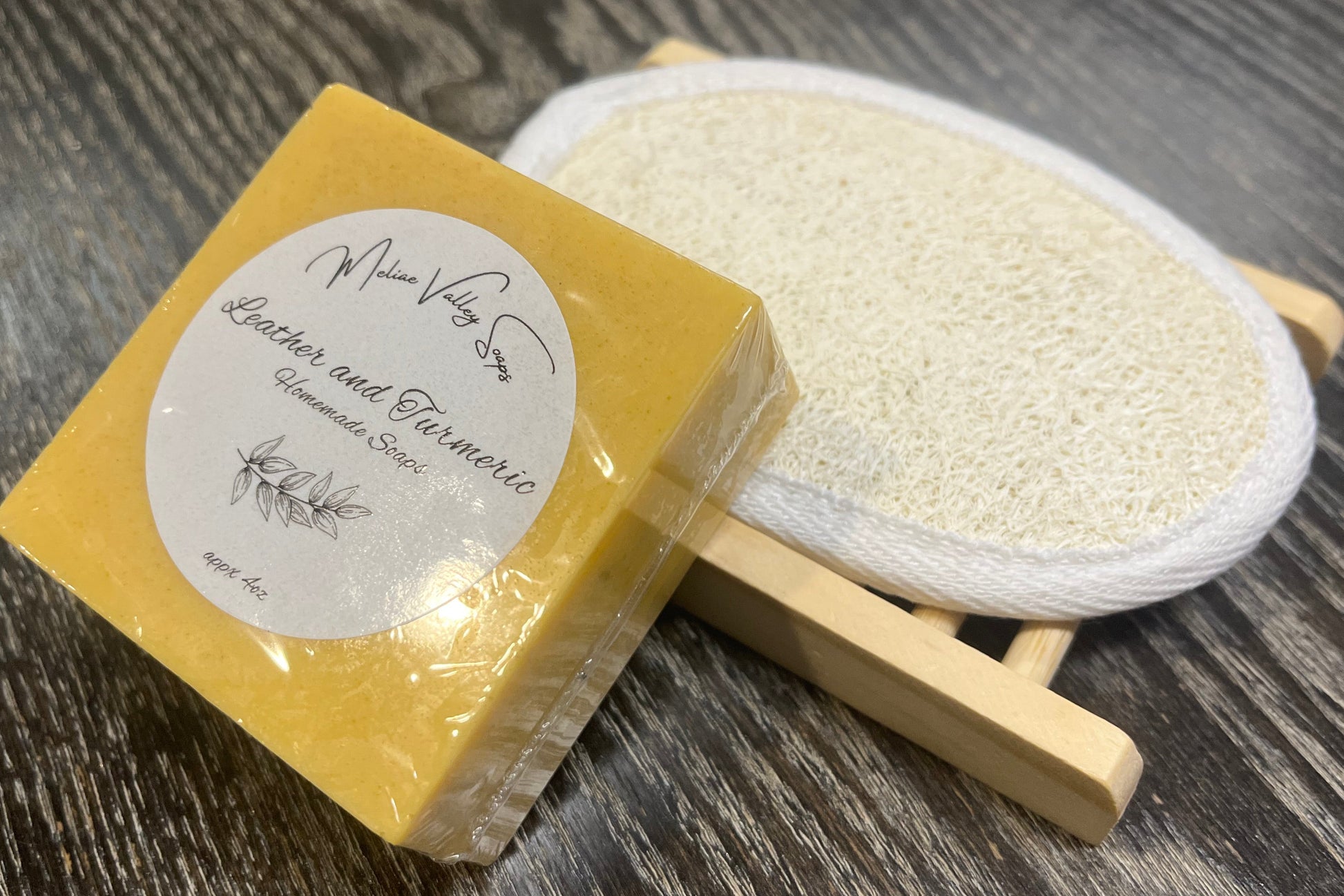 A yellow soap with a wooden stand and a loofah pad on a dark wooden surface. 