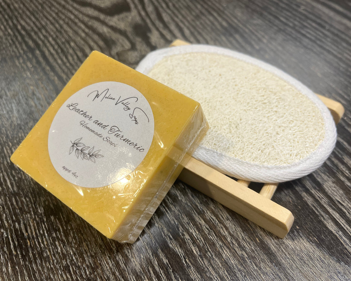 A yellowish-orange soap bar with a white sticker leans against a loofah pad and a soap bar holder.