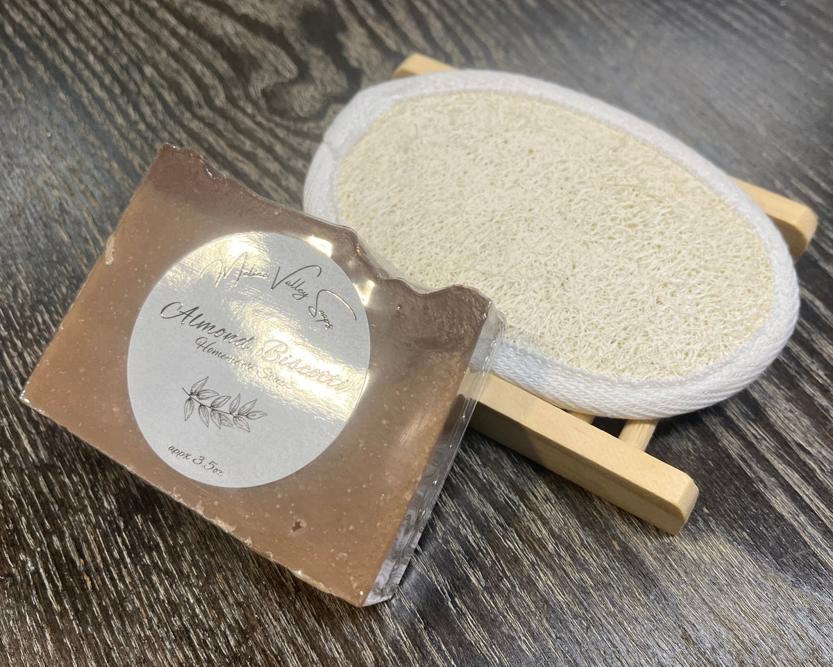 A brown soap bar with a white sticker leans against a loofah pad and a soap bar holder.
