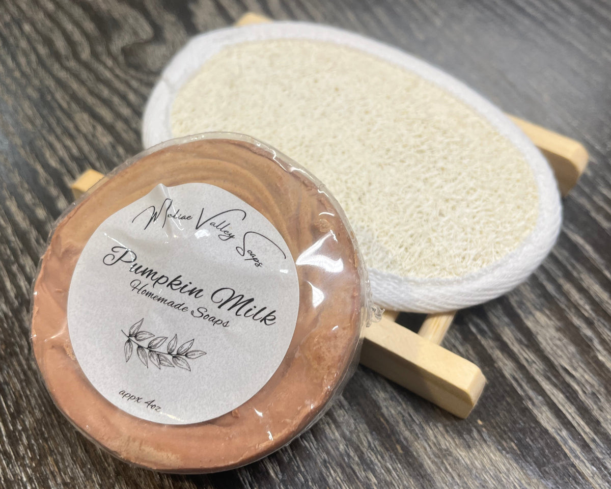 An orangey-brown soap bar with a white sticker leans against a loofah pad and a soap bar holder.