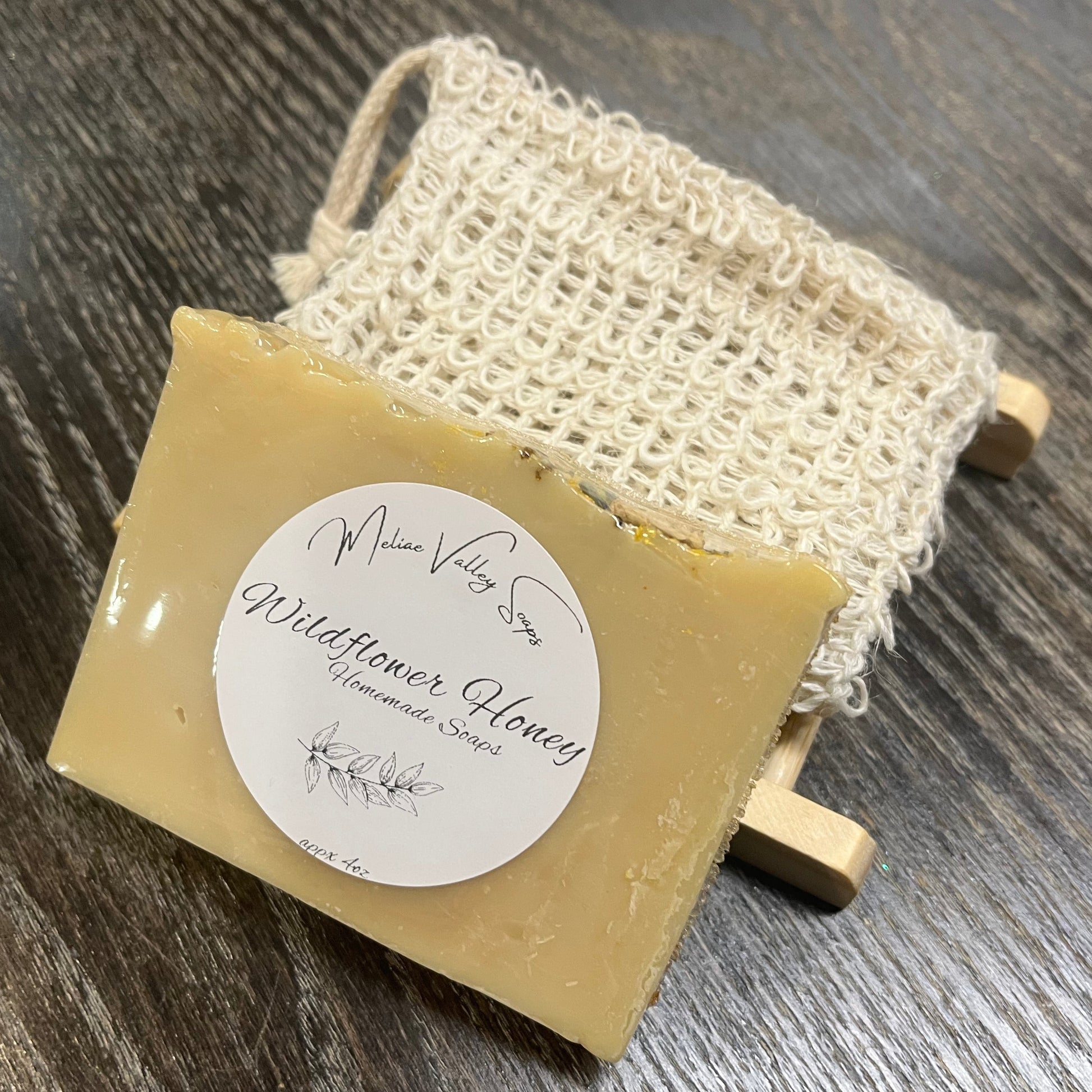 A yellow soap with a wooden stand and a exfoliating bag on a dark wooden surface. 