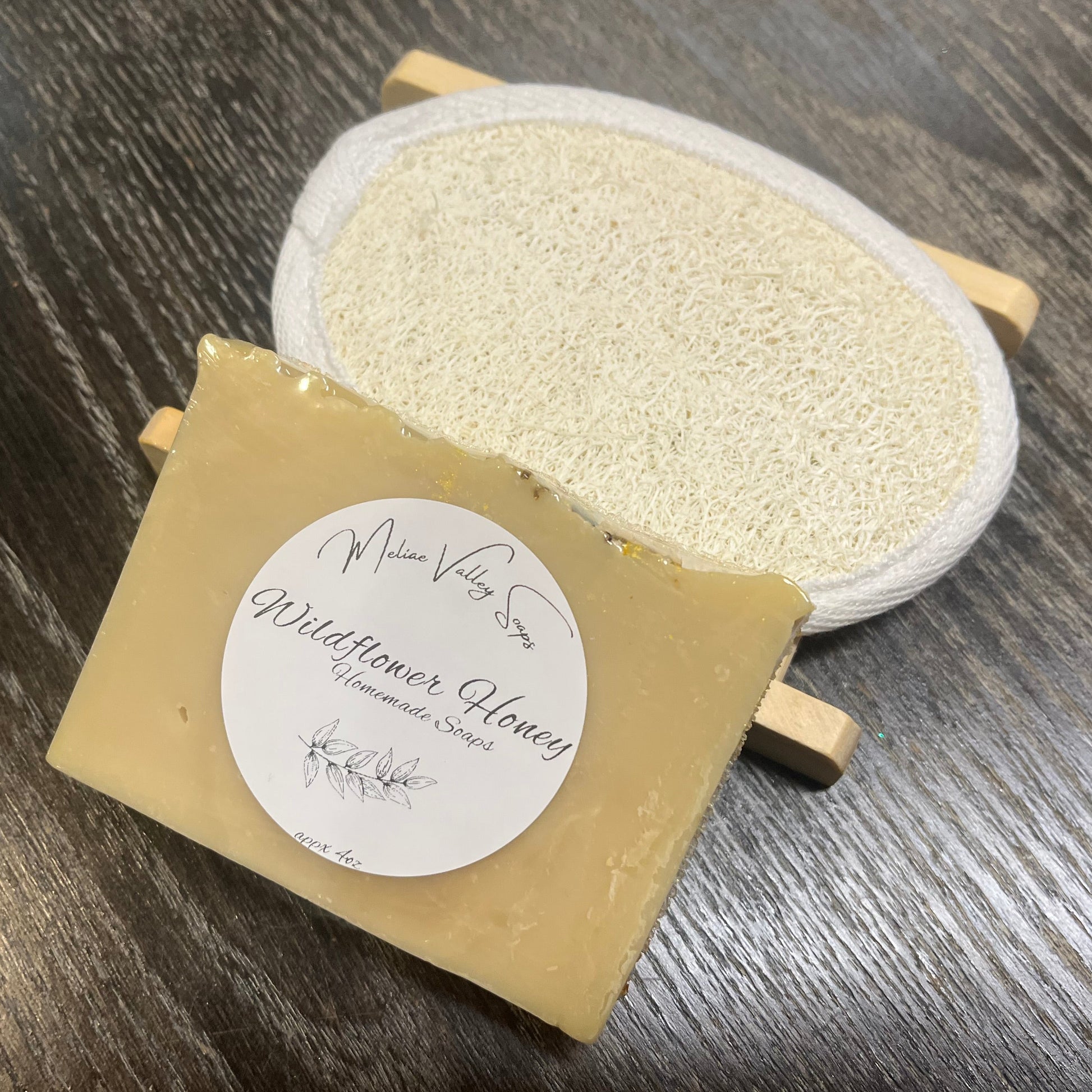 A yellow soap bar with a wooden stand and a loofah pad on a dark wooden surface. 