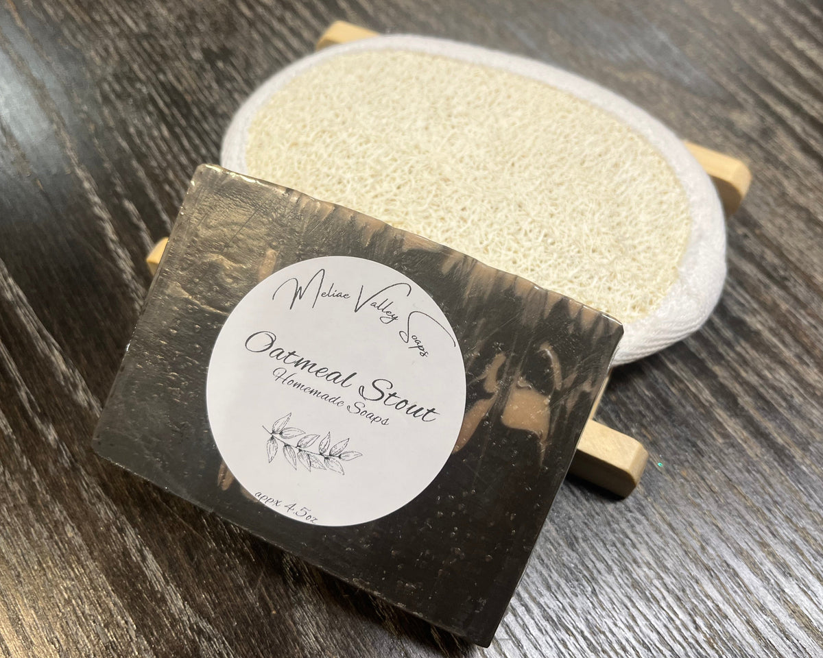 A beige and brown soap bar with a white sticker leans against a loofah pad and a soap bar holder.