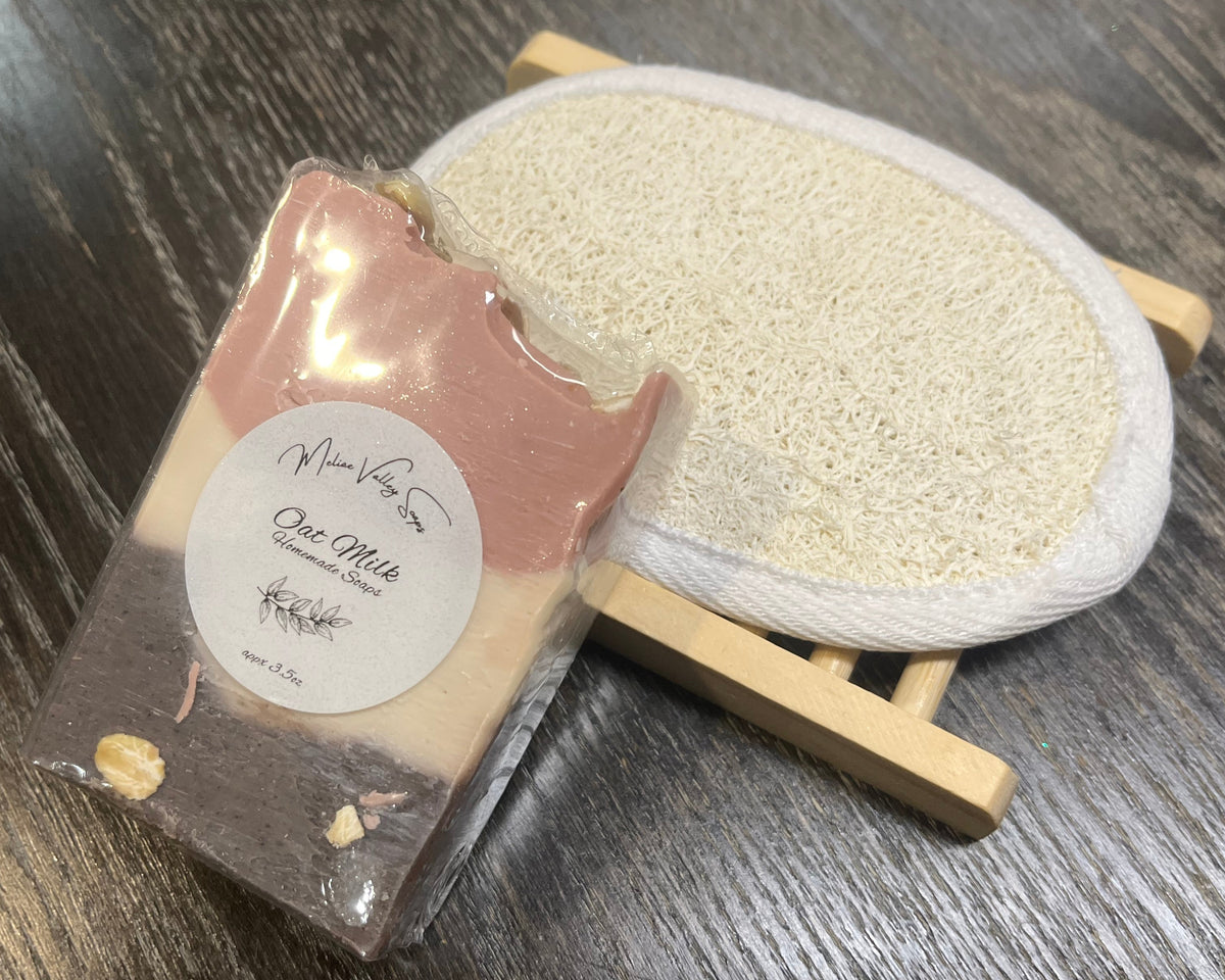 A beige, pink, and brown soap bar with a white sticker leans against a loofah pad and a soap bar holder.