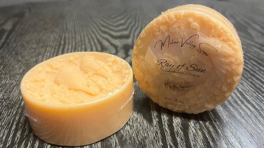 Two orange soaps with labels on a wooden surface.