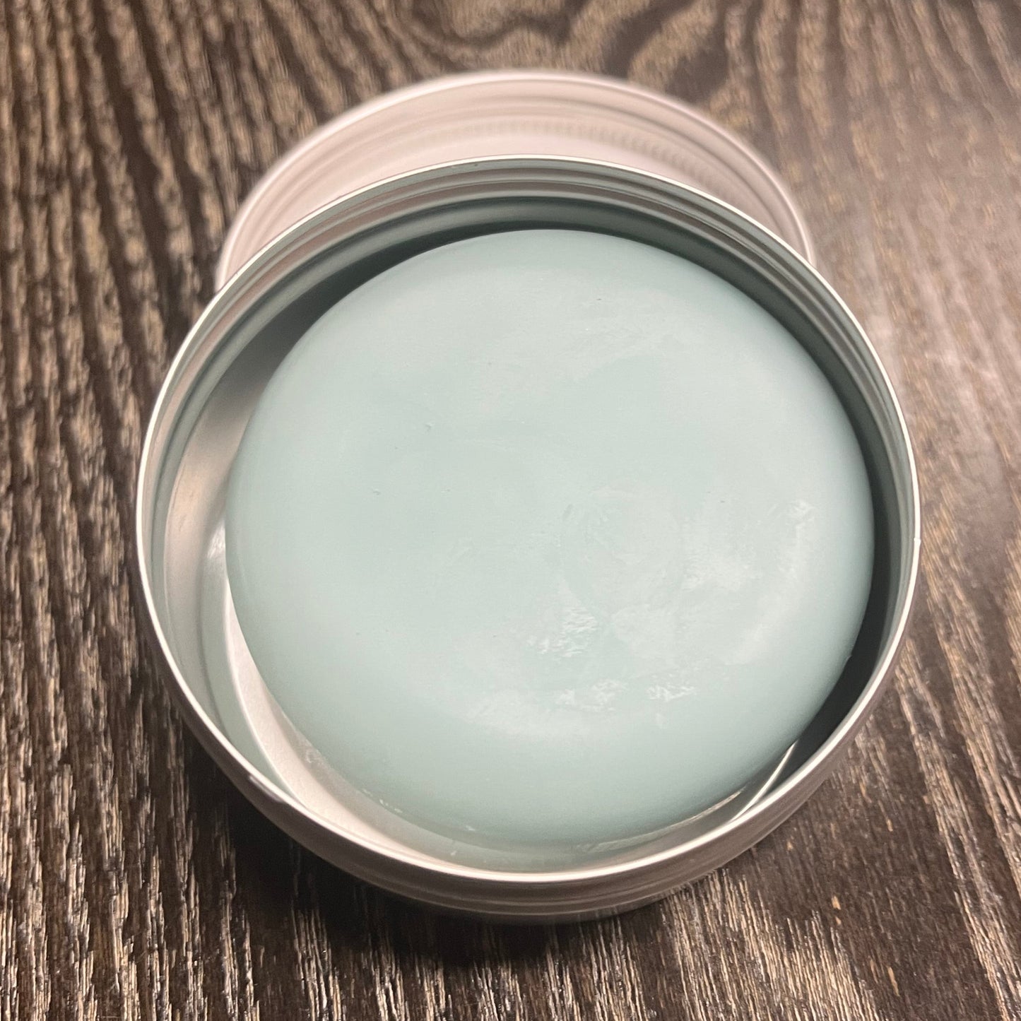 Light blue lotion bar in a metal tin on a wooden surface. 
