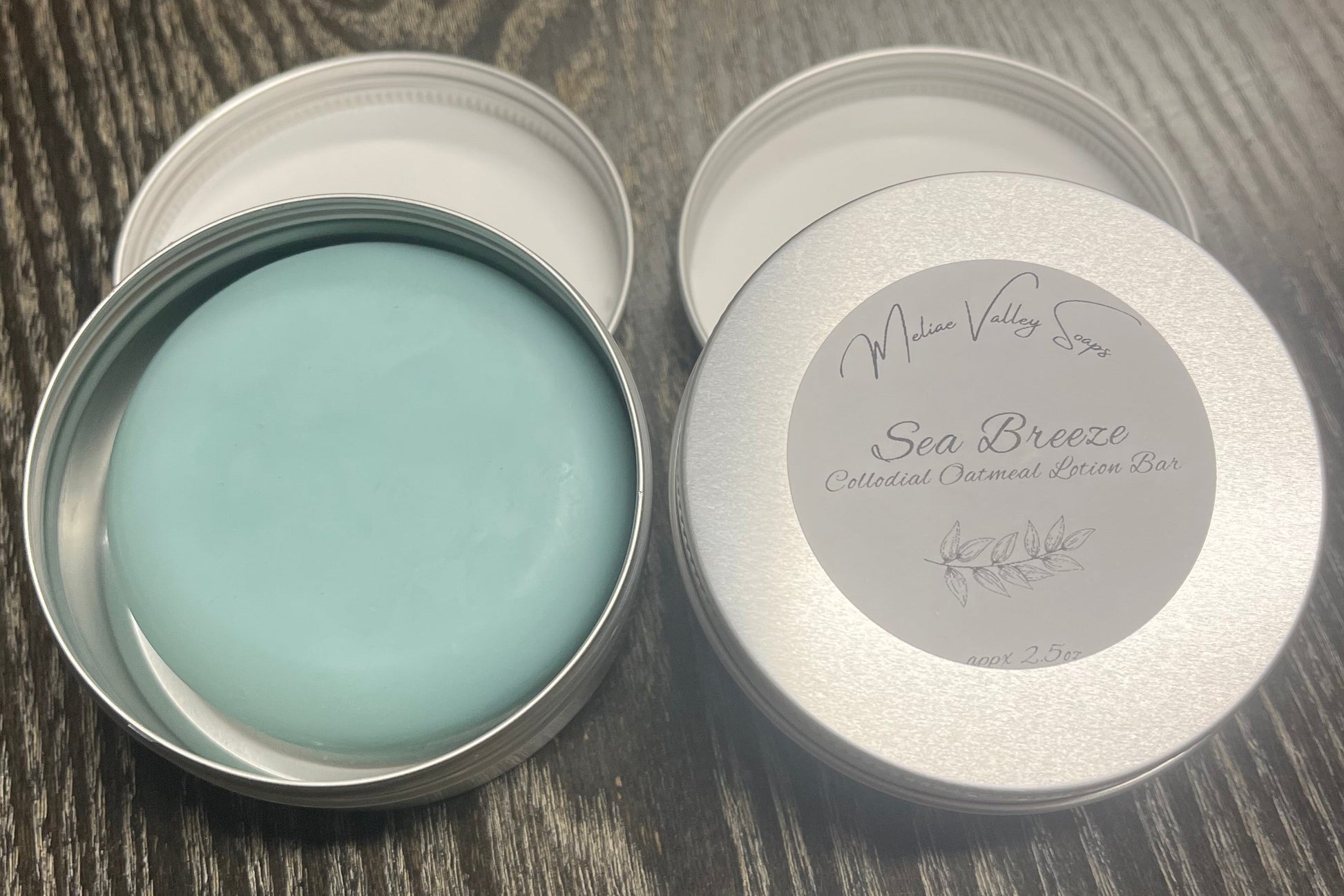Two tins of lotion bars sit on a textured surface, with one showing a beige lotion bar in a metal tin and the other with a white label, both set against a blurred background.