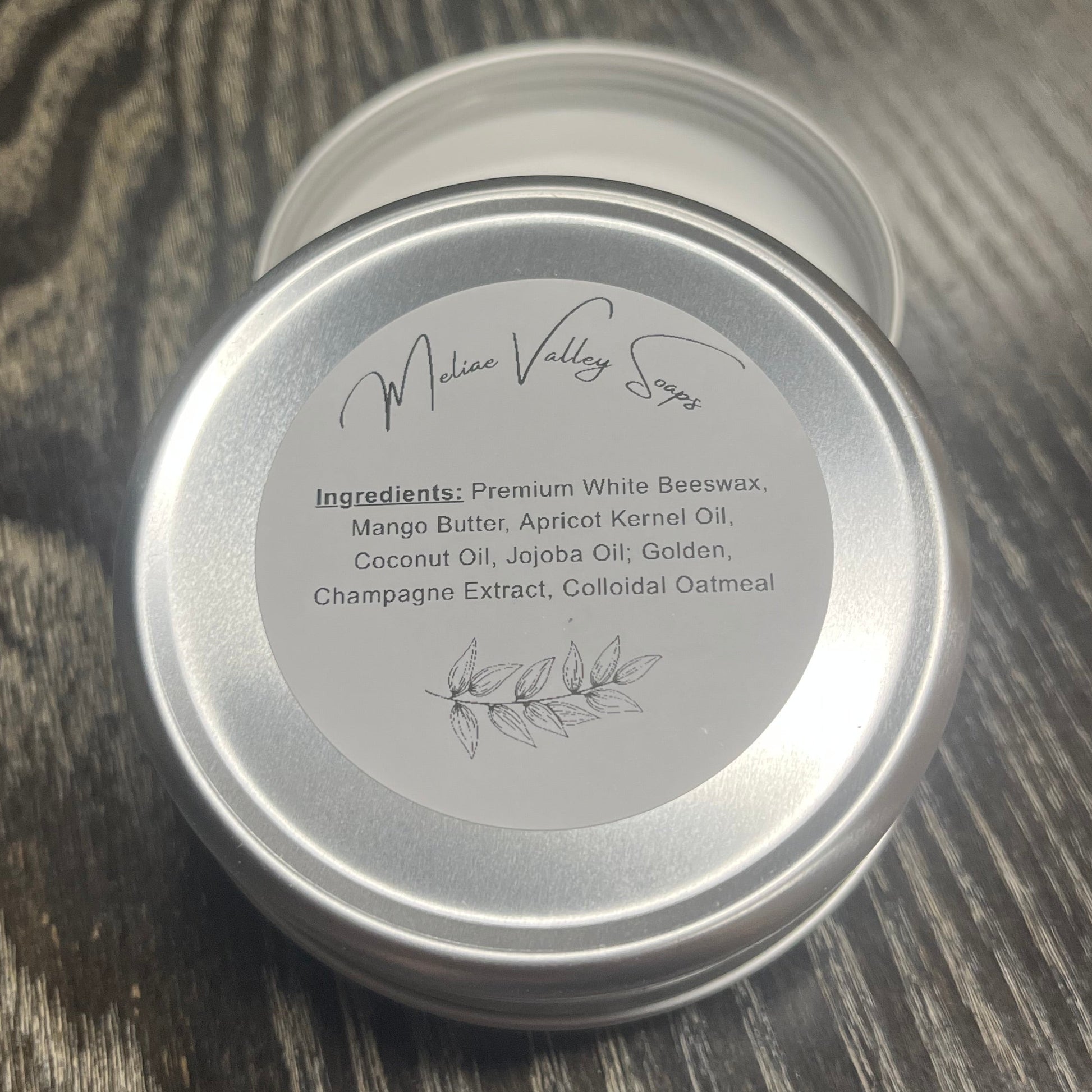 Tin of lotion bar with a white ingredients label on a wooden surface. 