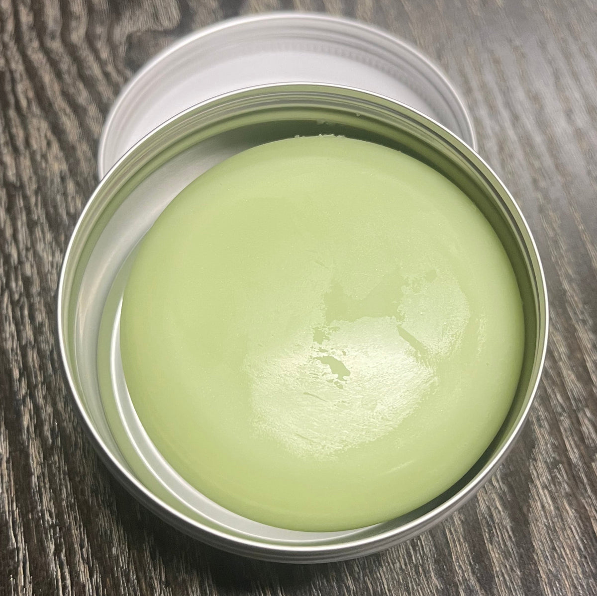 Light green lotion bar in a metal tin on a wooden surface. 
