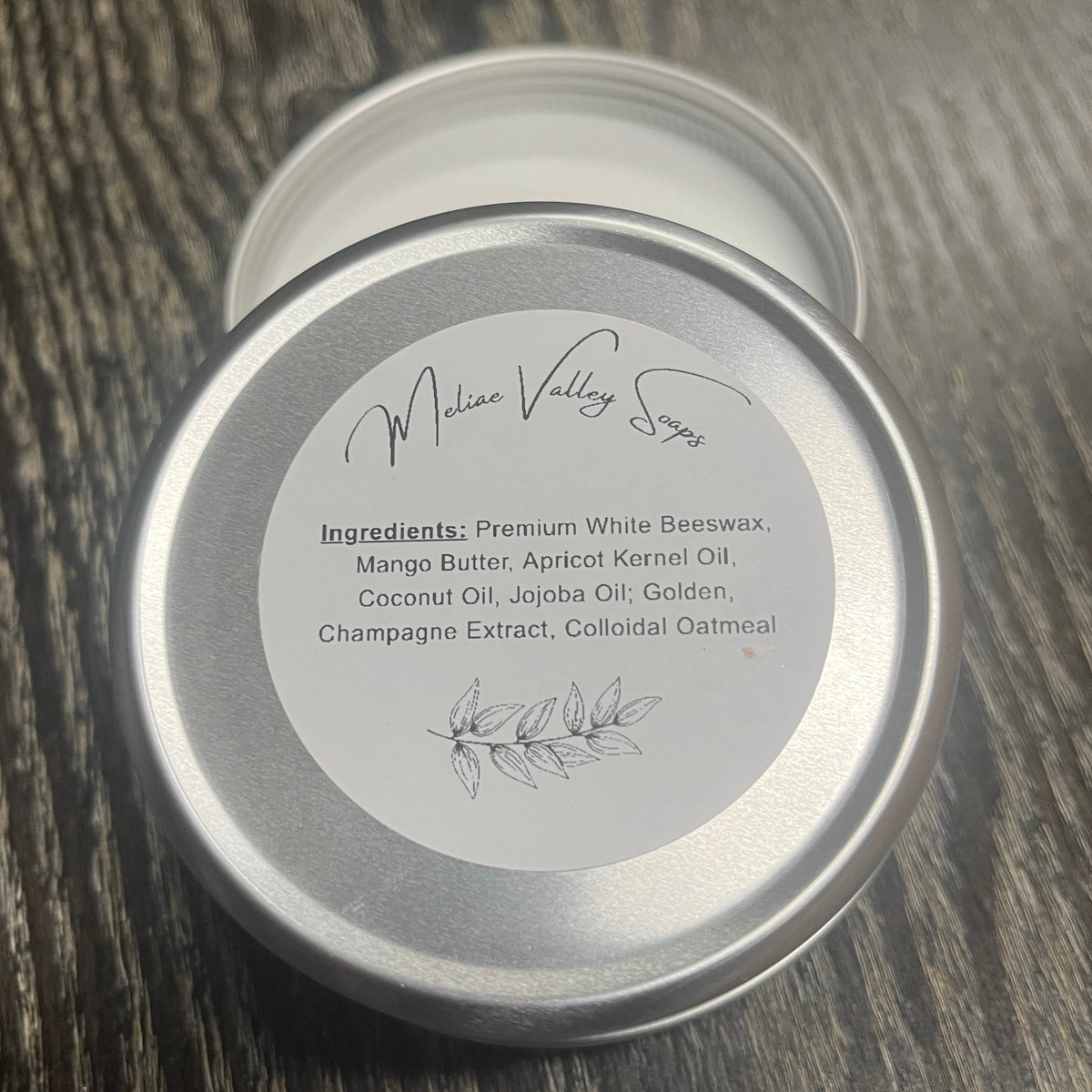 Tin of lotion bar with a white ingredients label on a wooden surface.