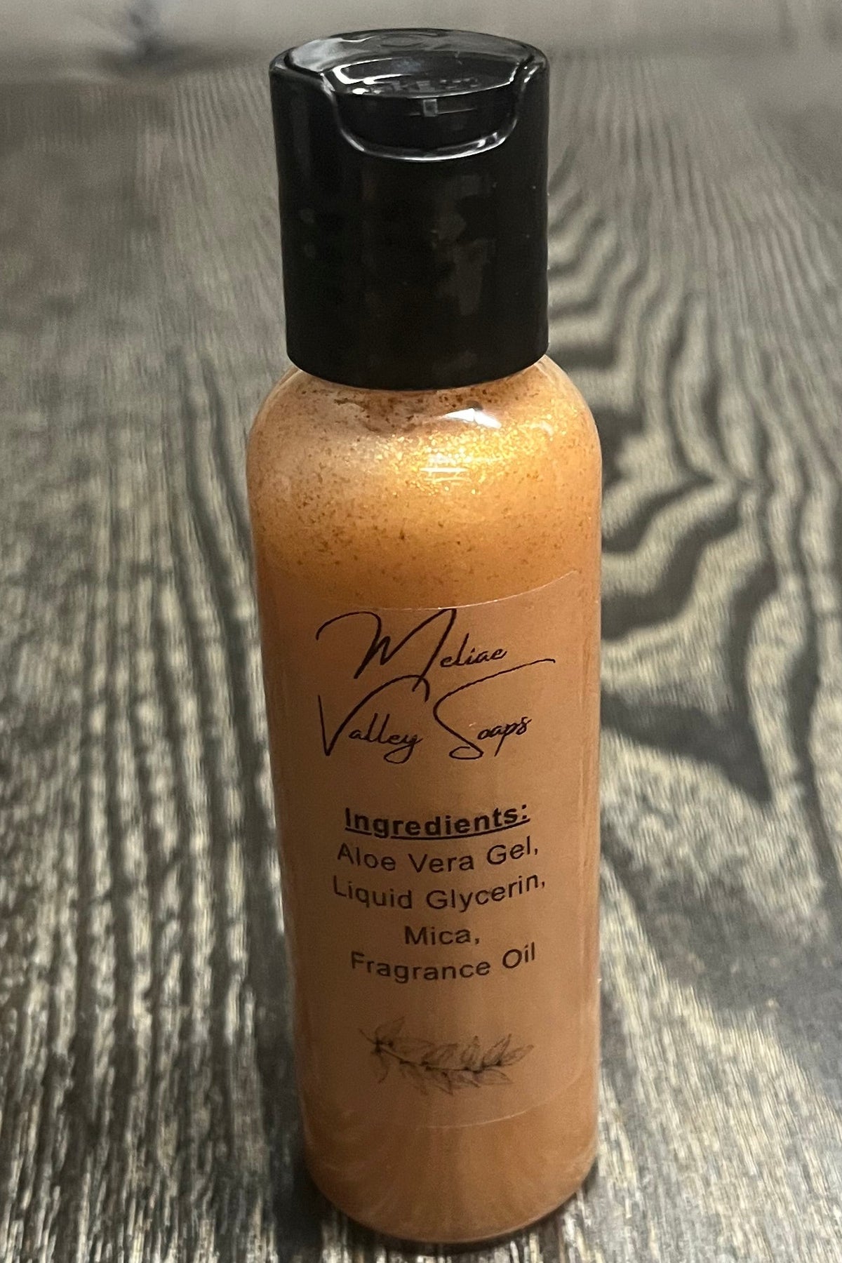 A small bottle of gold body shimmer with a clear ingredients label.