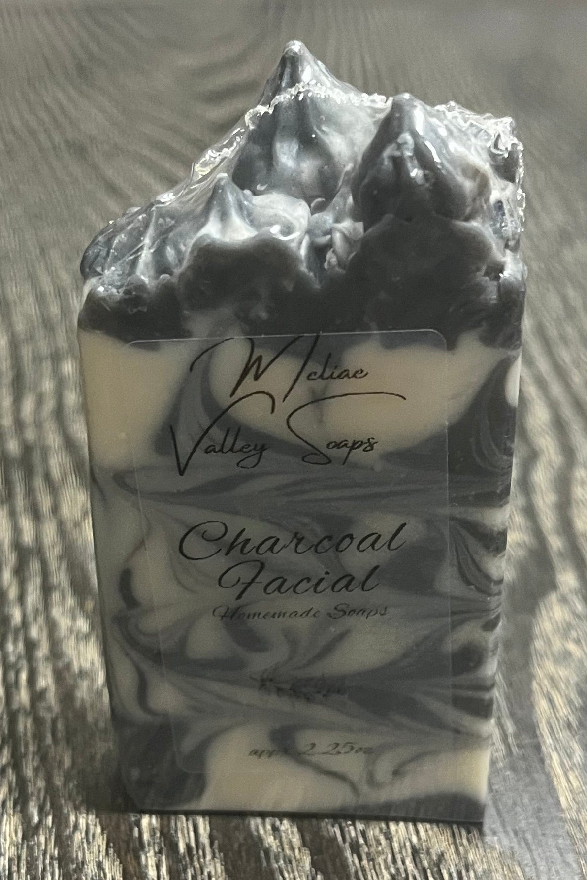 A handmade soap bar with black and white marbled swirls and a pointed top. It has a clear label on the front. 