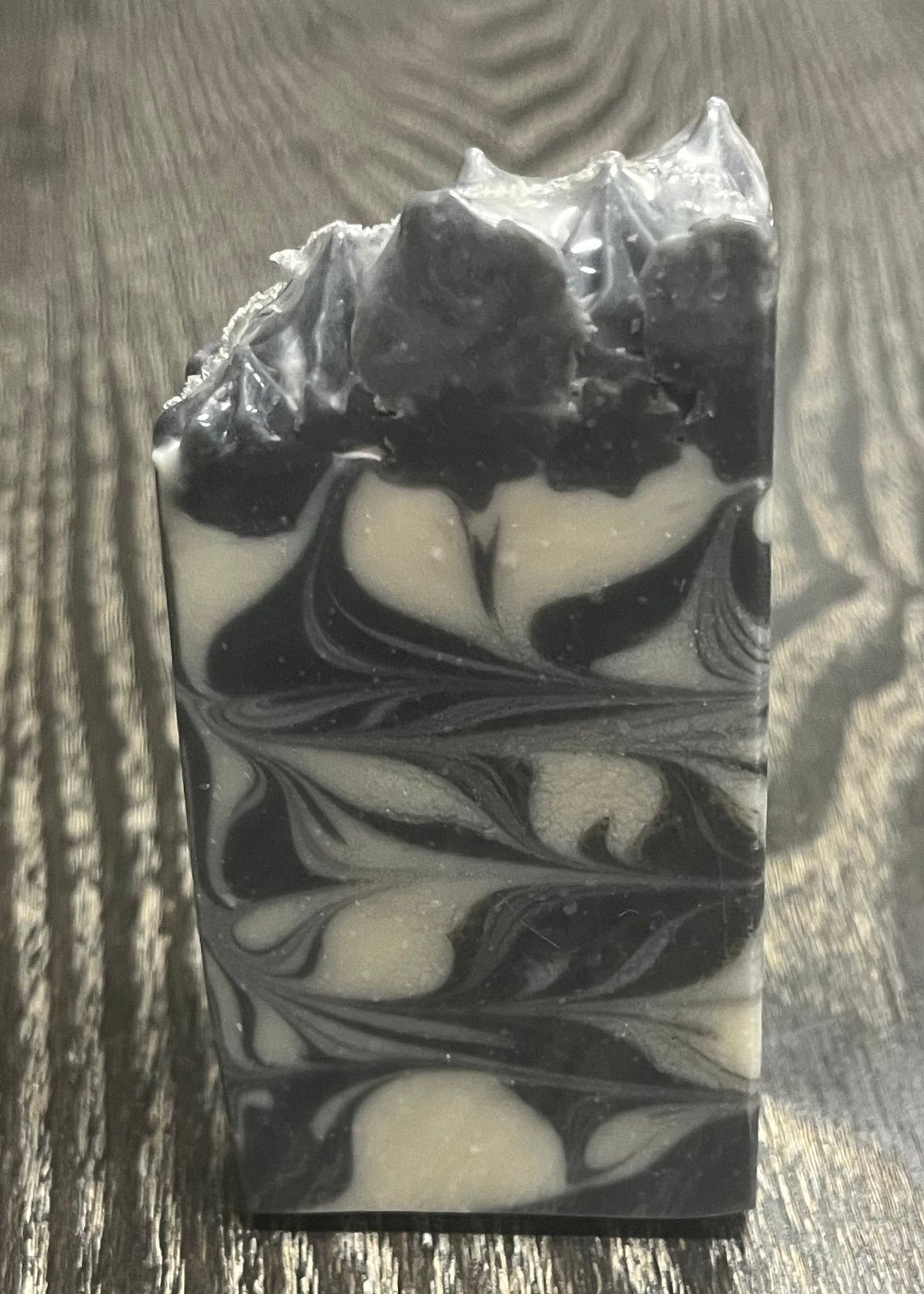 A handmade soap bar with black and white marbled swirls and a pointed top. 
