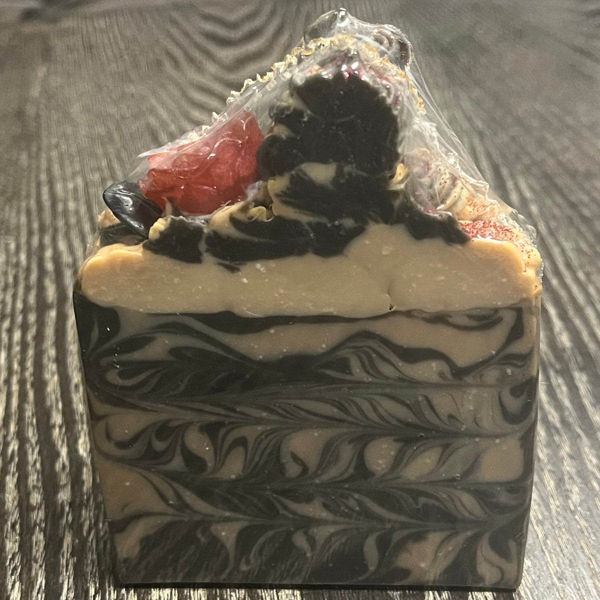 A rectangular bar of soap with a swirled black, gray, and cream pattern, topped with "soap frosting" and a small red rose. 