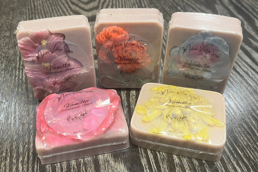 Five bars of light grey soap each with a different flower. Each flower has been made a different color. Each bar has a clear label on the front. 