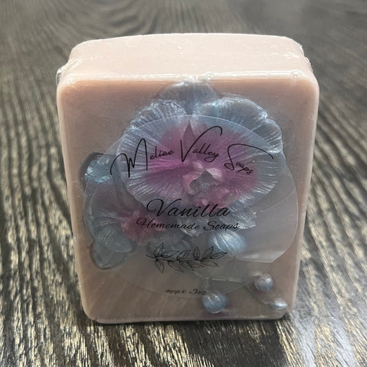 A bar of light grey soap with a blue and purple orchid flower. The bar has a clear label on the front. 