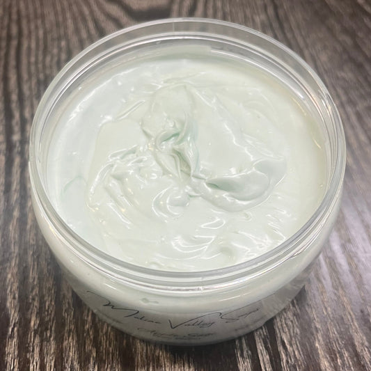 Jar of green whipped body butter. You can slightly see a clear label on the front from this angle. 
