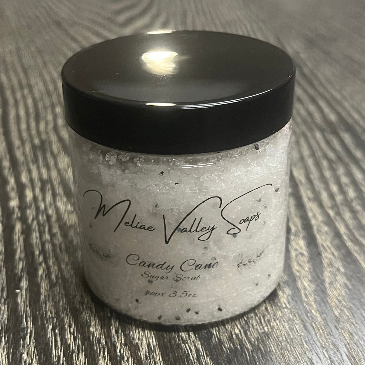 Jar of white sugar body scrub with a black lid and a clear label on the front.