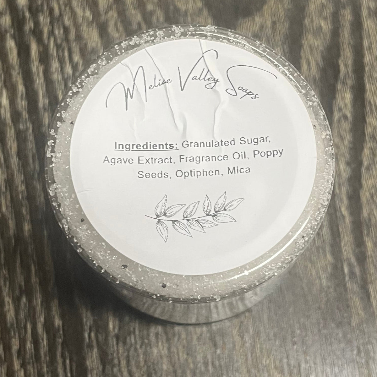 Jar of white sugar body scrub with a white ingredients label. 
