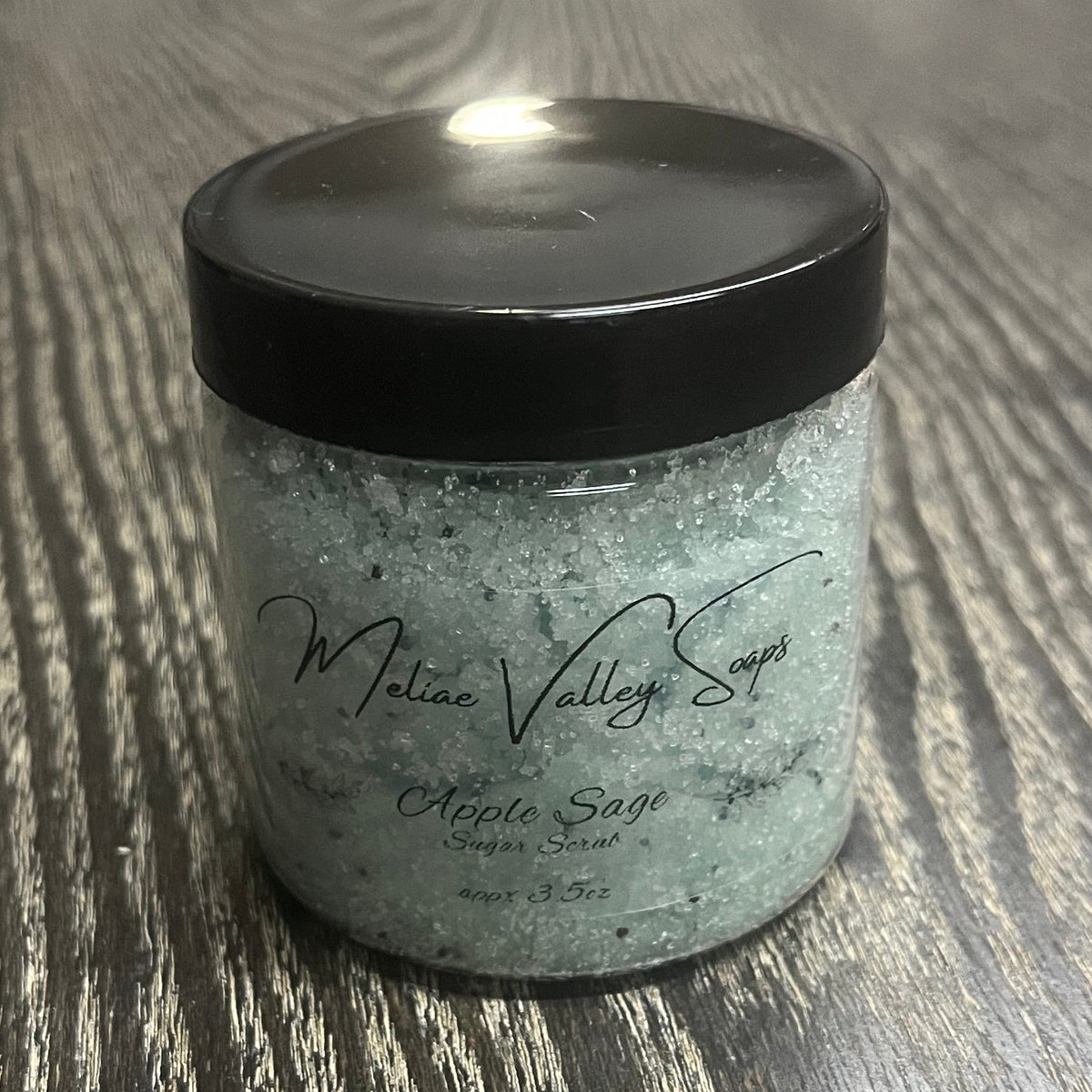 Jar of green sugar body scrub with a black lid and a clear label on the front.