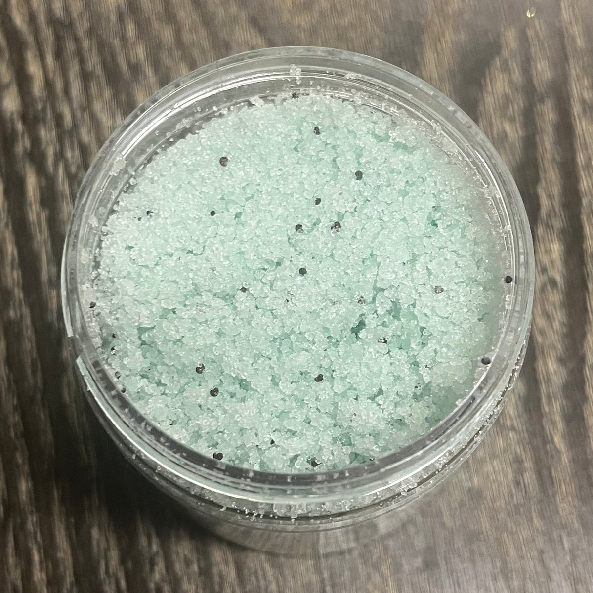 Jar of green sugar body scrub. You can slightly see a clear label on the front from this angle. 