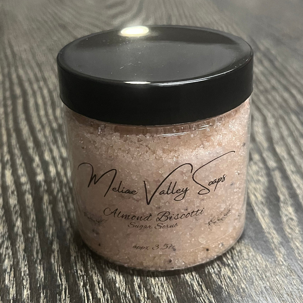 Jar of light brown sugar body scrub with a black lid and a clear label on the front.