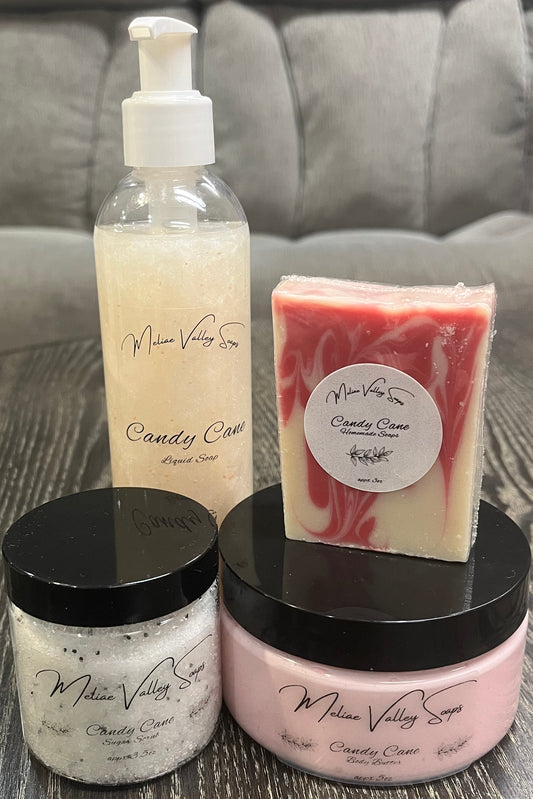 Two bottles next to each other. One has white whipped body butter; the other has a sugar scrub. On top of the body butter is a bar of soap. Behind the sugar scrub is a bottle of liquid soap. All four have labels on the front. 