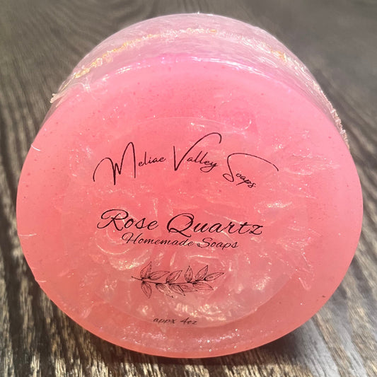 A round bar of clear pink soap with a design on the front. The design is dusted with white sparkles. The front of the bar has a clear label. 