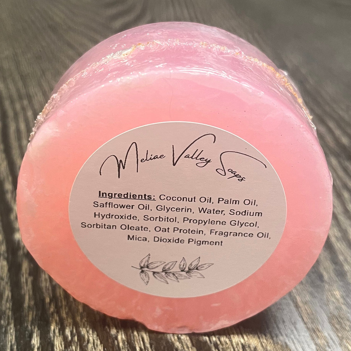 A round bar of clear pink soap. The bar has a white ingredients label. 