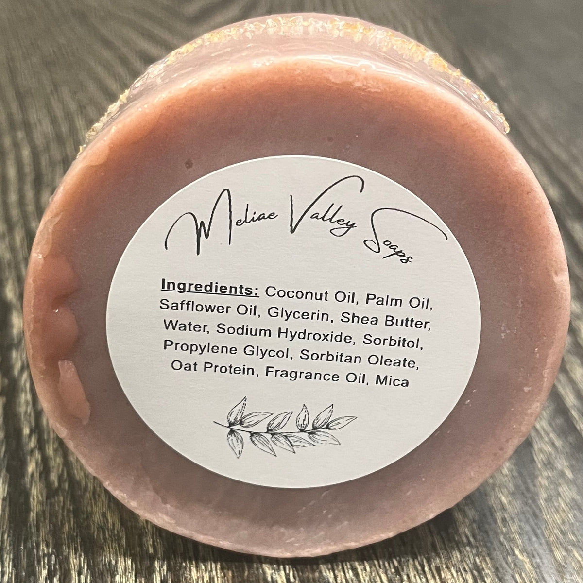 A dusty rose bar of soap. It has a  white ingredients label. 